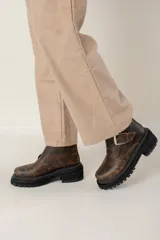 Bota corta de cuero con efecto gastado, diseño de puntera cuadrada y suela track robusta de goma negra. Presenta una hebilla metálica decorativa en el empeine y tirador en la parte trasera.