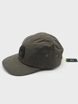 Gorra verde con visera plana y parche circular negro con logo de montaña.