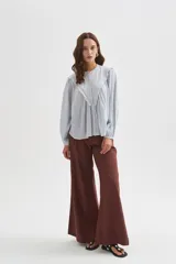 Blusa de algodón color celeste, de corte holgado y diseño con cuello a la base. Presenta mangas largas abullonadas, cierre frontal con botones y detalles de bordados en la pechera.