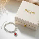 Pulsera de acero con cadena doble y dije redondo central que presenta una piedra roja tipo coral rodeada por un detalle trenzado.