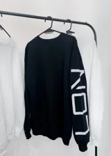 Buzo negro de corte holgado con inscripción blanca en la manga izquierda.