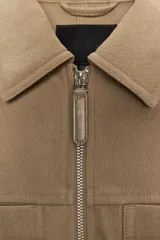 Chaqueta color tostado con cuello solapa, manga larga y cierre frontal con cremallera. Presenta bolsillos delanteros de plastrón con solapa y detalle de cintura ajustable con lazada.