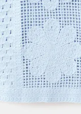 Chaleco celeste de punto con diseño de flores perforadas, sin mangas, escote redondo y cierre frontal con botones.