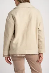 Campera de textura bouclé en color tostado, con diseño de solapas amplias, cierre frontal cruzado y mangas largas. Presenta un corte estructurado y moderno.