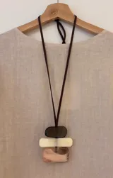 Collar con cinta de gamuza marrón regulable y colgante con tres piezas rectangulares de acrílico en color marrón oscuro, blanco y beige.