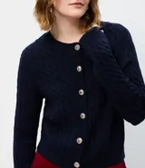 Cárdigan de punto trenzado color marrón, con cuello redondo, manga larga y cierre frontal con botones metálicos. Presenta puños y ruedo acanalados.