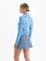Top de cuello polera y mangas largas, confeccionado en tela de punto con estampado de corazones atravesados por flechas sobre fondo azul. Presenta un diseño ajustado al cuerpo.