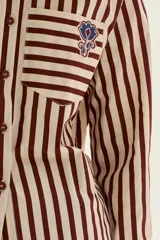 Camisa de manga larga con cuello y puños, confeccionada en tejido de rayas verticales en tonos crema y bordó. Presenta un bolsillo de parche en el pecho con un bordado exclusivo.
