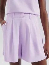 Short de sastre color lila, de tiro alto, con pliegues frontales y cierre de botones visibles en la cintura.