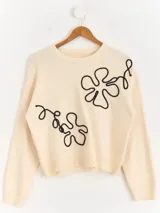 Sweater de punto color marrón chocolate con diseño floral bordado en cordón color crudo. Presenta cuello redondo, mangas largas y puños acanalados.