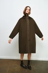 Parka oversize de corte recto confeccionada en tejido con mezcla de lana en color verde oliva. Presenta cuello alto con capucha, cierre frontal con botones y bolsillos laterales. Incluye detalles en tejido acolchado a contraste en la solapa frontal y puños.