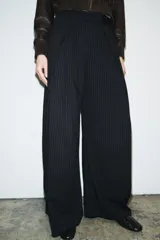 Pantalón de tiro medio con diseño de raya diplomática, corte wide leg y detalle de pinzas en el delantero. Cuenta con cintura con trabillas, bolsillos laterales y cierre frontal con cremallera, botón y ganchos metálicos.