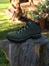 Botín de trekking color verde oliva, confeccionado en cuero, con cordones reforzados, ganchos metálicos y suela de goma negra con relieve antideslizante.