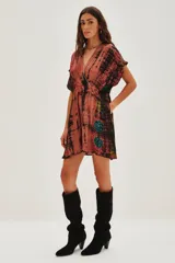 Vestido midi de viscosa con escote en V profundo, mangas cortas tipo kimono y cintura elástica con lazo ajustable. Presenta un estampado tie-dye en tonos rojizos, negros y toques de verde, con aplicaciones decorativas brillantes.