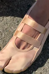 Bailarina de diseño tipo tabi con separación para el dedo, confeccionada en una combinación de gamuza y material textil en tono rosado. Presenta doble tira elástica sobre el empeine, tirador en el talón y suela plana de goma en color tostado.