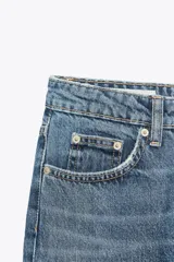 Jeans de tiro alto con diseño de cinco bolsillos, trabillas para cinturón y cierre frontal con cremallera y botón metálico.
