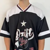 Camiseta estilo fútbol americano de corte oversize, color negro con detalles en blanco y bordó en el cuello y mangas. Presenta un estampado frontal con tipografía desgastada, una estrella y un escudo.