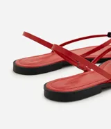 Sandalias planas rojas con diseño de dedo, tiras finas y aplique metalizado decorativo.
