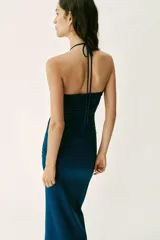 Vestido midi de color azul marino con escote halter y tirantes finos ajustables. Presenta un diseño con drapeados frontales y laterales, detalle cut out en el pecho con fornituras metálicas doradas y falda de corte evasé.