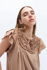 Remera color beige con escote fruncido con volados y lazos, de mangas cortas con volados.
