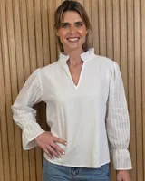 Blusa blanca de algodón con mangas largas abullonadas semitransparentes con detalles bordados y puños con volados. Presenta cuello mao con volados y escote en V.