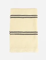 Bufanda tejida color beige con dos franjas horizontales negras en cada extremo y flecos en los bordes.