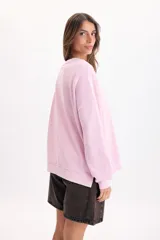 Buzo rosa de corte holgado y diseño liso, con cuello redondo, mangas largas y puños ajustados.