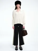 Sweater de tejido de punto color beige, con diseño de trenzas en el frente y mangas lisas. Presenta cuello polo con escote en V y puños y ruedo acanalados.