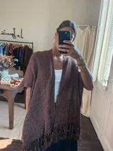 Ruana abierta de tejido de punto con acabado brillante y flecos en el ruedo. Presenta mangas cortas y un diseño holgado y versátil.