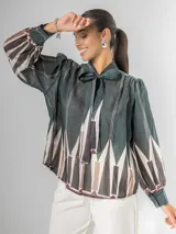 Camisa de manga larga con cuello alto y lazo para atar, confeccionada en tela liviana con estampado geométrico en tonos verde oscuro, blanco, beige y marrón.