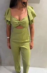 Mono largo color verde oliva, con escote corazón y detalle de nudo en el centro del busto. Presenta aberturas laterales en la cintura y mangas cortas con volados en capas.