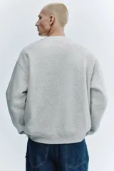 Buzo de cuello redondo en mezcla de algodón color gris melange, con diseño bordado frontal que incluye texto y el dibujo de un caracol.