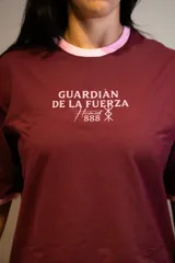 Remera oversize color bordó con cuello y puños de rib de color rosado. Estampado frontal en rosado con el texto "GUARDIÁN DE LA FUERZA" y otros símbolos.