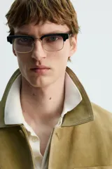 Cazadora de hombre de corte relajado, confeccionada en piel con acabado ante color mostaza/verde oliva. Presenta cuello solapa, manga larga con puño abotonado, cierre frontal de botonadura y cuatro bolsillos de plastrón visibles (uno en el pecho y tres en la parte inferior).