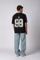 Remera de algodón color blanco con corte regular, cuello redondo y mangas cortas. Presenta detalles de líneas finas negras en los hombros y estampado gráfico frontal con tipografía y logotipos en color negro.