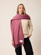 Pashmina de textura suave y color crema, con diseño liso y terminaciones en flecos en los extremos. Incluye una etiqueta decorativa en una de las esquinas.
