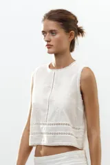 Top blanco de algodón con cuello redondo y sin mangas. Presenta bordados a tono y cierre trasero con abertura y botón.