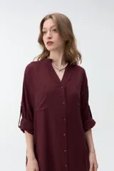 Vestido largo color bordó, tipo camisero, con cuello mao, escote en V y cierre frontal con botones. Mangas largas con vuelta y diseño holgado.