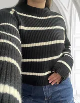 Sweater de punto grueso negro con rayas horizontales blancas, cuello alto y corte holgado.