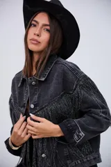 Campera de jean color negro con efecto lavado, de corte oversize, con flecos brillantes integrados en el diseño frontal y en las mangas.