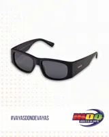Lentes de sol MDQ modelo Vayu, color negro con lentes grises. Diseño rectangular con patillas anchas y logo de la marca en el lateral.