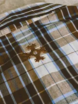 Camisa de manga corta con corte híbrido boxy fit/oversize, confeccionada en algodón. Disponible en tres diseños: a cuadros marrones, a rayas blancas y negras, y a rayas burdeos y blancas. Presenta bordados de diseño propio de la marca.