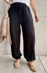 Pantalón negro tipo babucha con cintura elástica fruncida y cordón ajustable, corte holgado y puños elásticos en los tobillos.