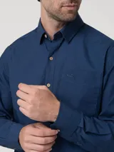 Camisa de manga larga RKF modelo Galiton, confeccionada en popelina de algodón orgánico. Presenta cuello clásico con botones, cierre frontal con botones de madera, bolsillo en el pecho con logo bordado y mangas ajustables con trabilla.