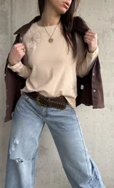 Remera manga larga de color beige, con cuello redondo y diseño bordado de flores en el hombro y lateral.