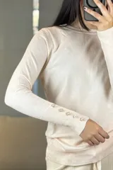 Buzo de hilo negro con cuello redondo, manga larga y detalle de botones decorativos en los puños y a lo largo del antebrazo.