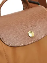 Mochila Longchamp modelo Le Pliage Original en tamaño M, color verde oscuro. Presenta solapa y asas de cuero marrón con cierre de botón a presión, correas ajustables de tela y cierre superior con cremallera.