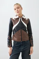 Chaqueta corta de cuero sintético color negro, marrón y blanco, con cuello de piel sintética blanca, cierre frontal con cremallera y bordado en las mangas.
