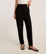Pantalón zanahoria de poliéster y elastano color negro, de tiro alto, con cierre tradicional, bolsillos traseros y botón metálico con efecto martillado.