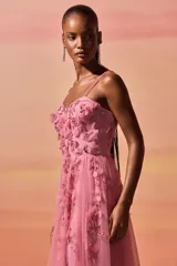Vestido largo de fiesta color rosa, con cuerpo tipo corsé y falda de tul con caída fluida. Presenta flores en 3D y bordados artesanales en el escote y el torso, con breteles finos.